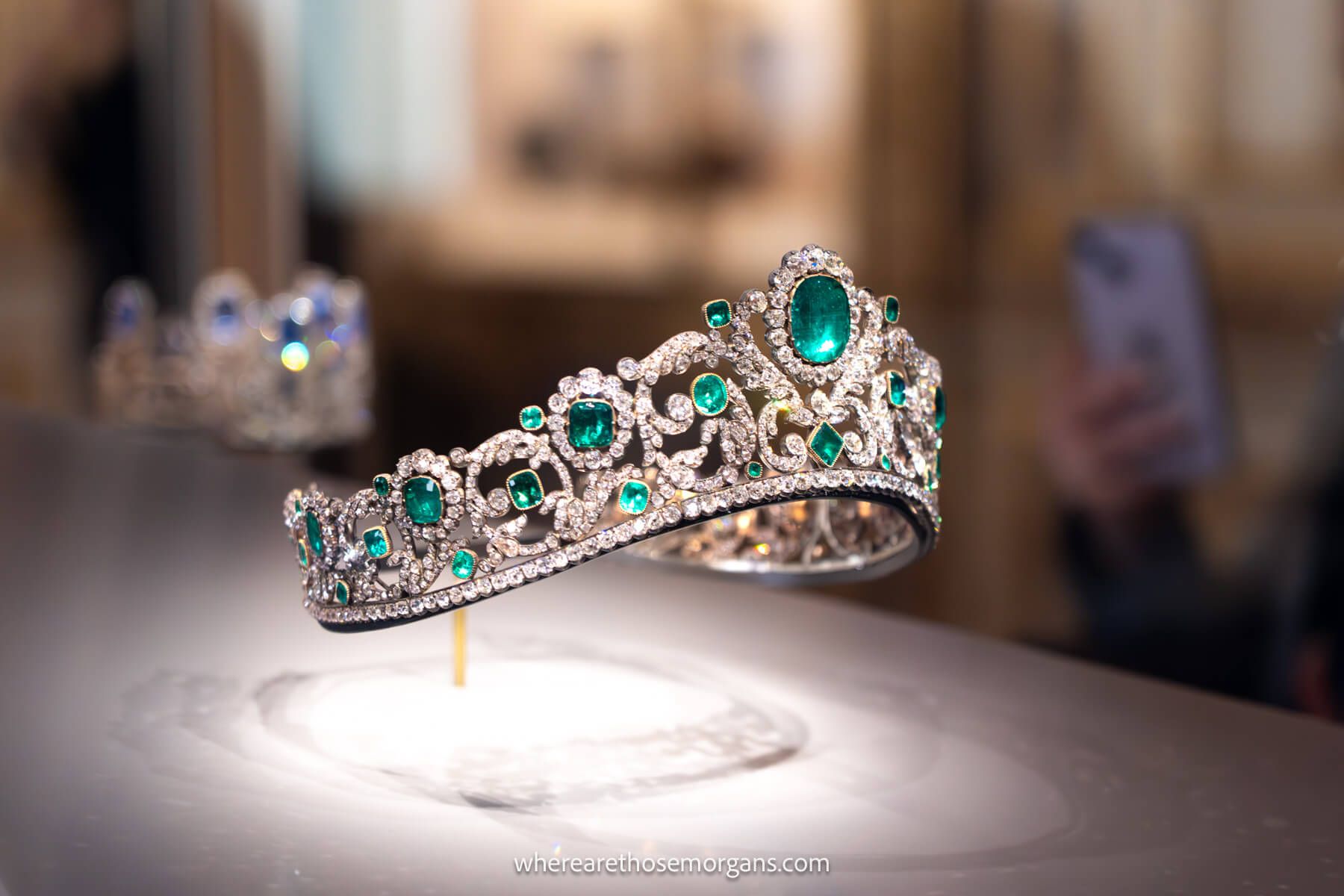 Photo of a crown with green jewels in a glass exhibit inside the Louvre Museum
