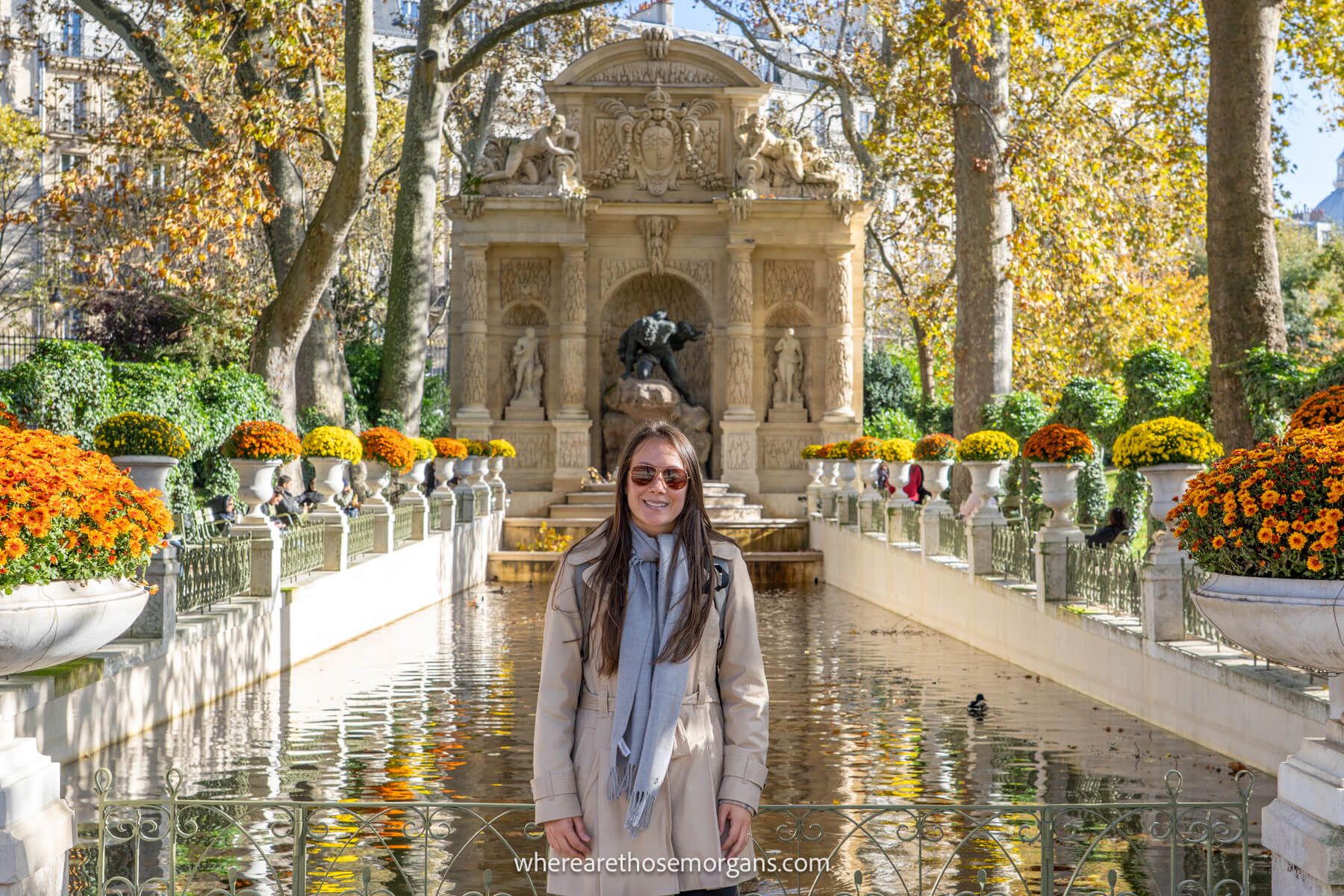 Photo of a tourist standing in front of a fountain with flowers in a park on a sunny but cool day