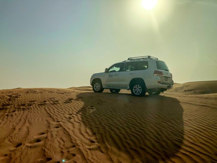 a 4x4 parked on a sand dune with the sun showing in the background