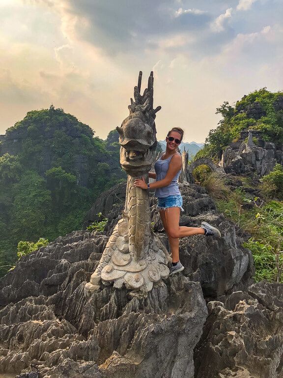Kristen sticking back leg up holding onto stone statue of dragon at Mua Cave viewpoint