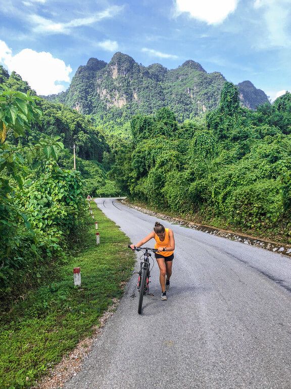 Woman pushing her bike up a steep hill near Phong Nha