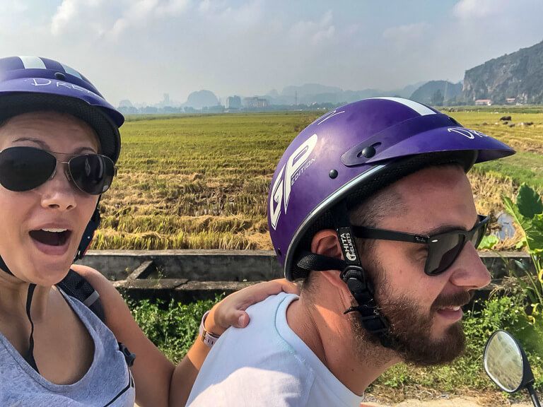 Side shot of Mark and Kristen on a motorbike with rice paddies background