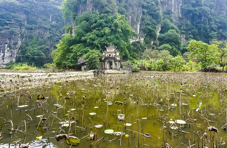 Lotus pond with path cutting across to gated entrance of Bich Dong pagoda