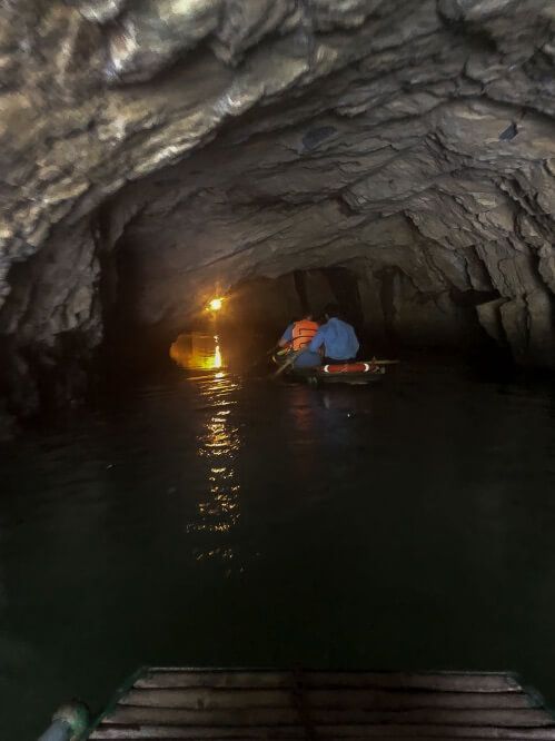A single boat gliding through a cave on a river in the dark with one light shining in the distance