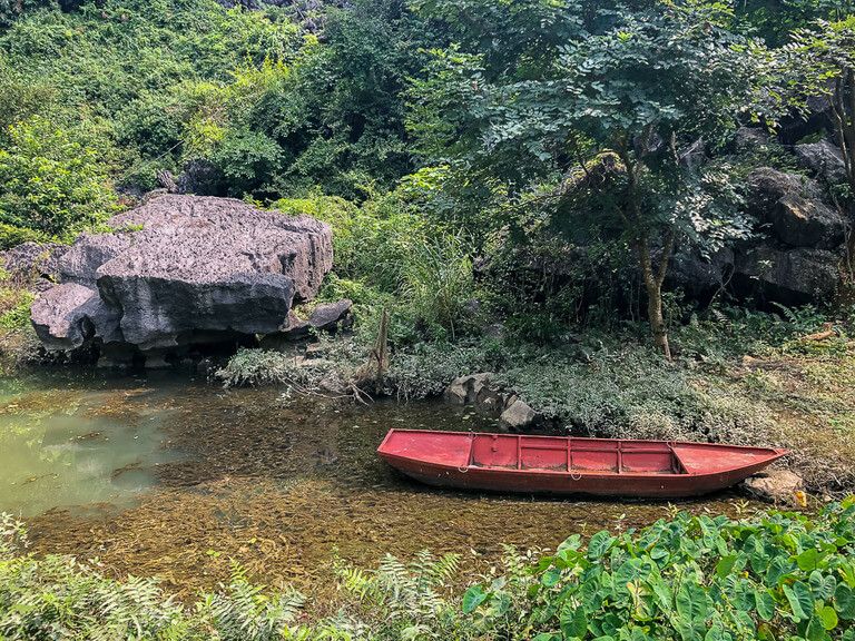 Red boat in shallow lake surrounded by green vegetation Bich Dong Tam Coc