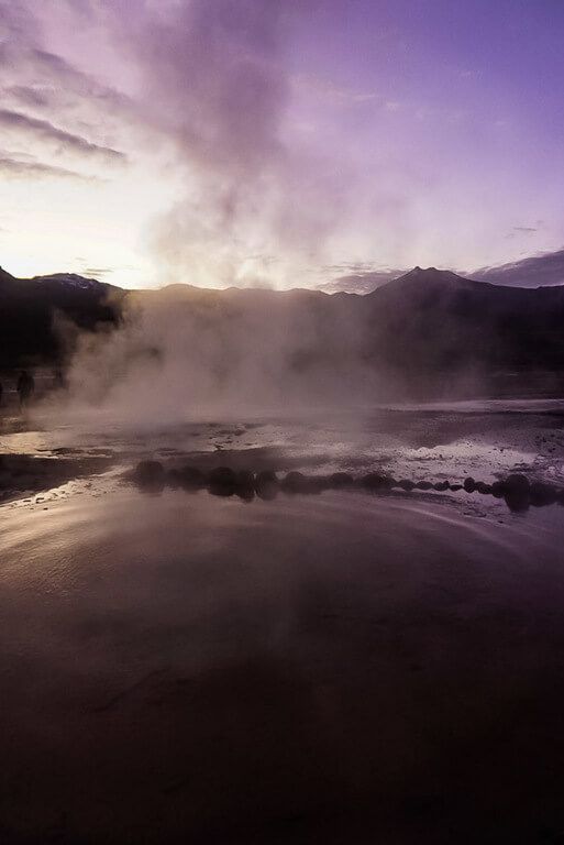 Still water reflecting early morning purple color through steam at el Tatio geysers