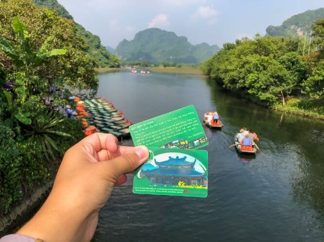 Two entrance tickets for the Trang An boat tour in front of boats gliding down the river