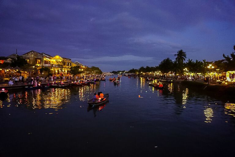 Boats on  Thu Bon River at night with the banks lit up