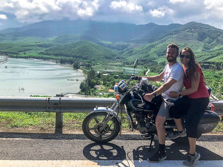 Mark and Kristen on Dr Phu motorbike with green hills and lake background