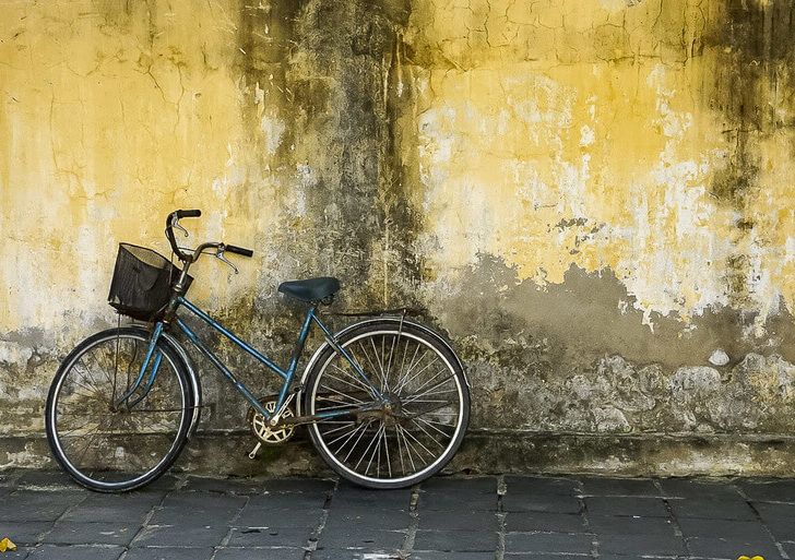 Blue bicycle leaning against yellow wall in Hoi An Vietnam How to get from da nang to Hoi An
