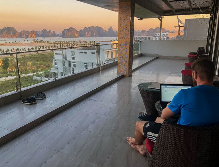 mark working on laptop on balcony with amazing view of Halong Bay at dusk