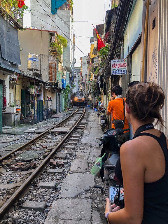 Train appearing round a bend on train track down train street in hanoi people tightly packed against wall