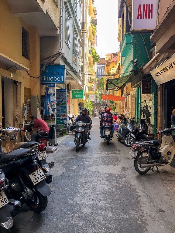 2 motorbikes pass each other on narrow alleyway road in hanoi Vietnam