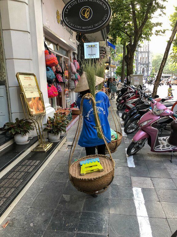 woman carrying fruit baskets on sidewalk in Vietnam