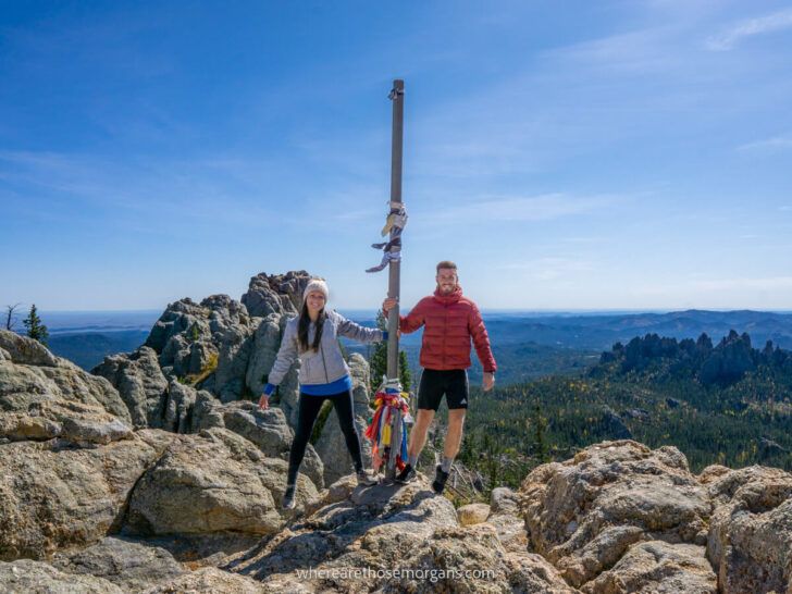 Couple holding a pole marking the summit of Black Elk Peak Trail in South Dakota after hiking the old Harney Peak path