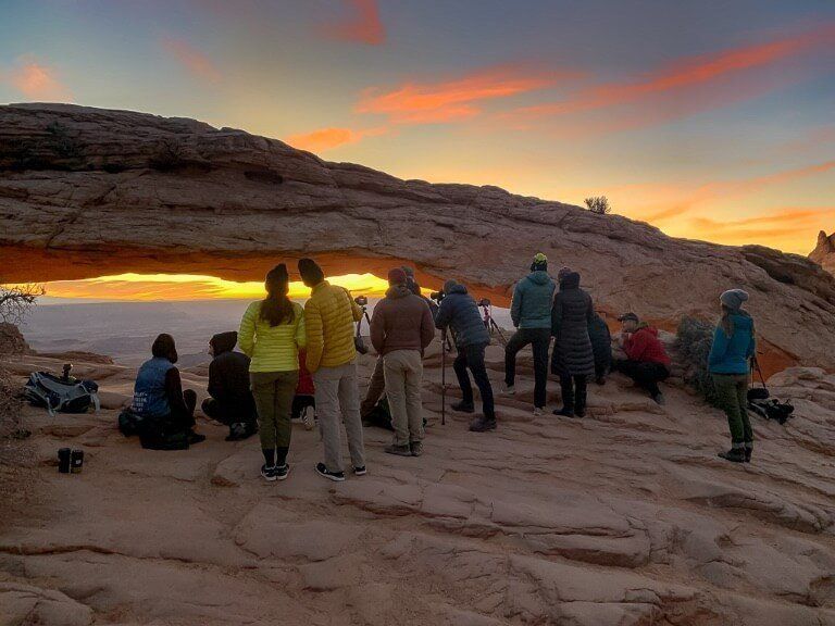 Small crowd of photographers in a line at Mesa Arch Canyonlands watching sunrise over the canyon