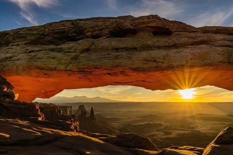Mesa Arch sunrise glowing red with beautiful sunburst cutting through a hazy canyon floor