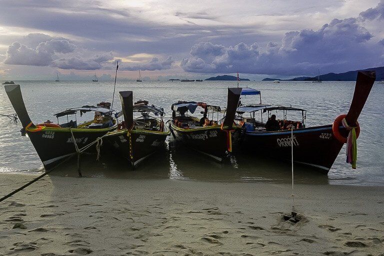 4 long tail boats lined up along sunset beach Thailand