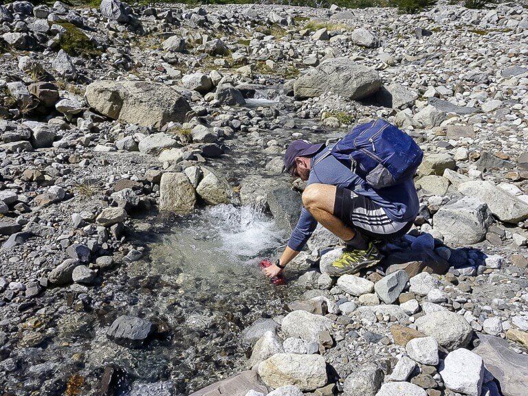 Mark filling water bottle up in a mountain river W Trek Chile hiking tips for beginners