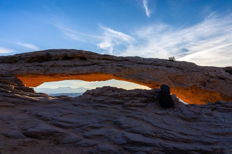 Mesa Arch glowing red from bright sunrise sun behind clouds