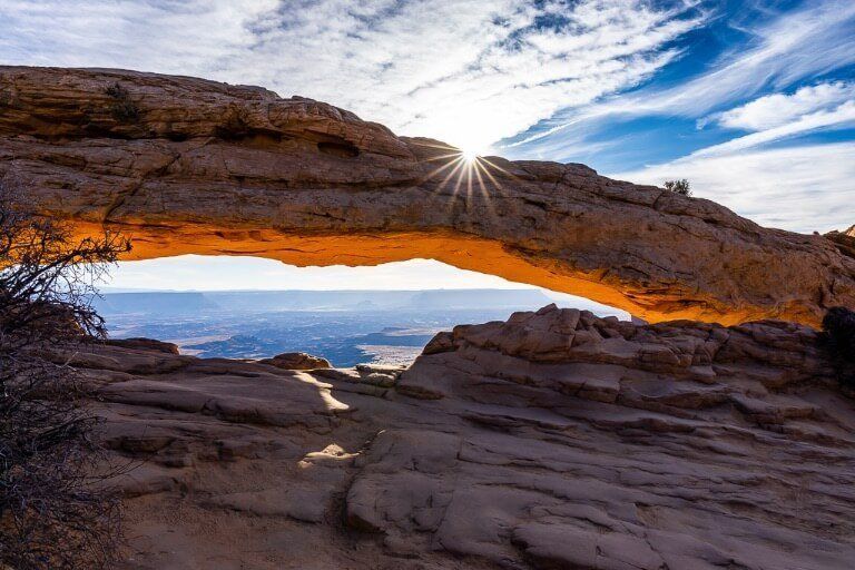 Mesa Arch after sunrise with deep blue sky glowing rock and sunburst