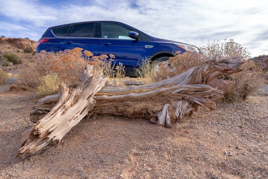 Car on a road behind a log with gravel on the ground