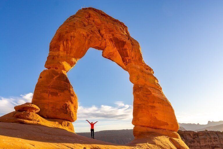 Kristen standing underneath huge towering rock formation in Utah