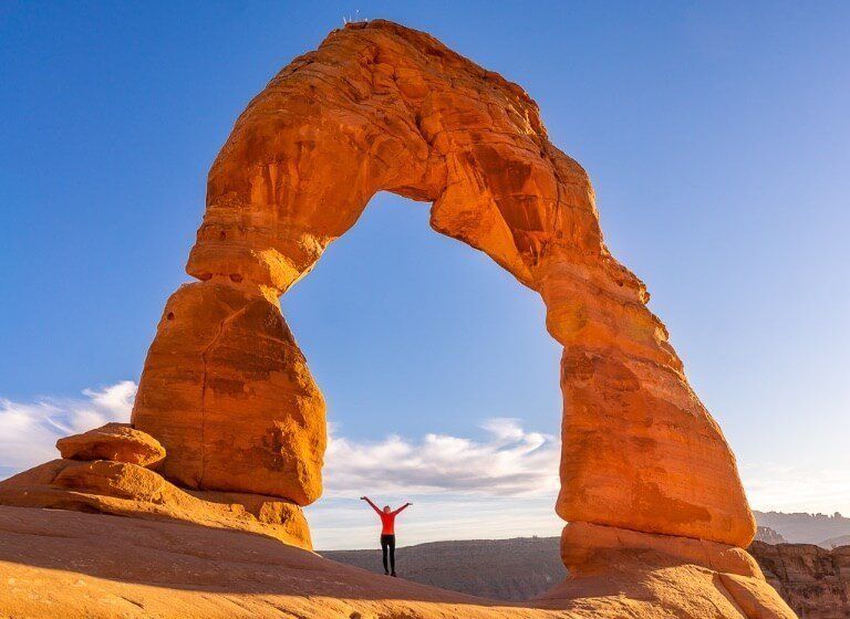 Kristen standing underneath Delicate Arch during the day dwarfed by the huge size of the arch