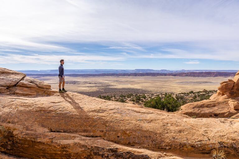 Man stood on huge orange rock with amazing valley view in background