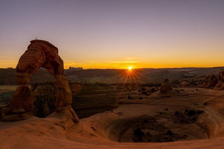 Sunset over Delicate Arch and bowl sun setting in horizon deep orange and purple sky