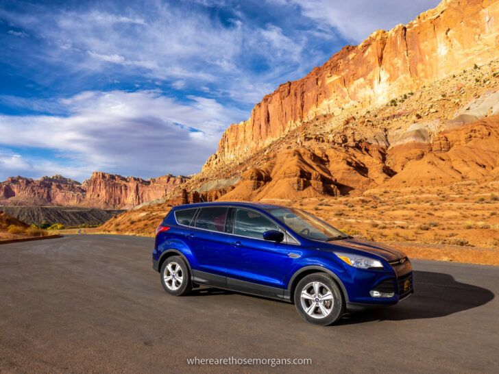Blue car parked on Capitol Reef scenic drive against orange sandstone rocks driving the best Utah road trips