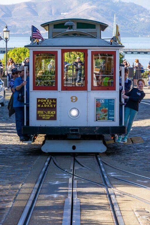 Iconic San Francisco cable car from the front and people hanging out must visit on sf itinerary