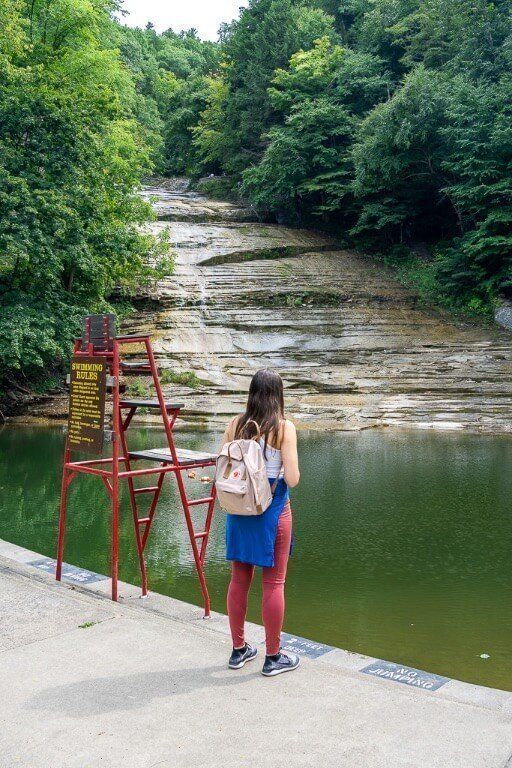 Kristen stood next to a life guard seat in front of a swimming pool at the bottom of a waterfall