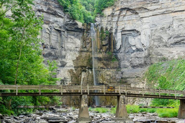 Taughannock Falls State Park Waterfall running dry after Summer drought deep green foliage and cool wooden bridge foreground near Ithaca NY finger lakes