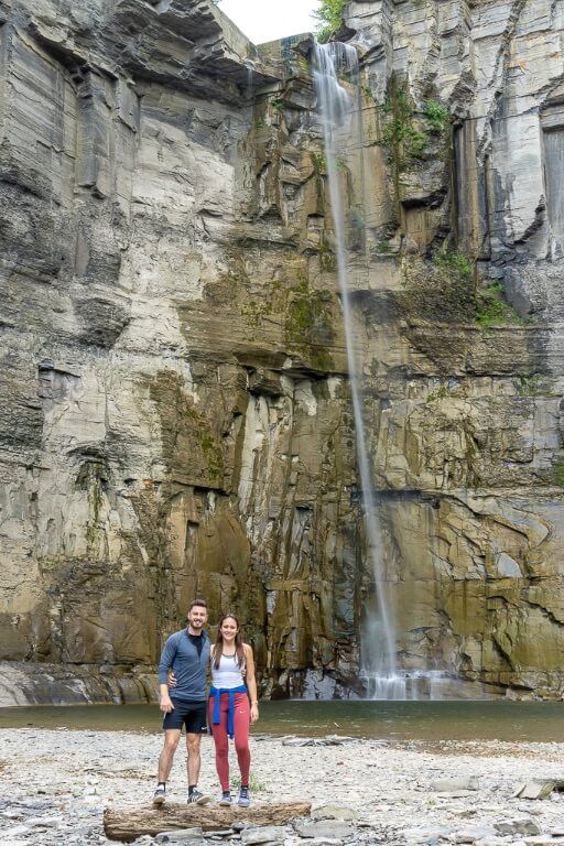Mark and Kristen stood on a log in front of towering Taughannock Falls waterfall Ithaca NY state park
