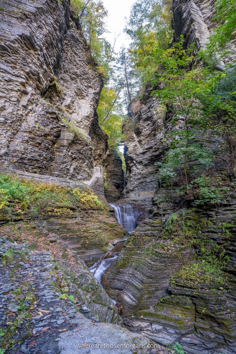 View through narrow gorge with tall walls and wispy waterfalls cascading