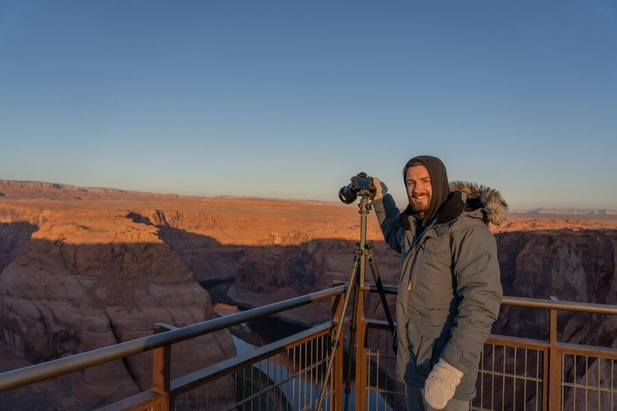 Photographer in winter coat and gloves taking photos of a rock formation with blue sky on a cold morning