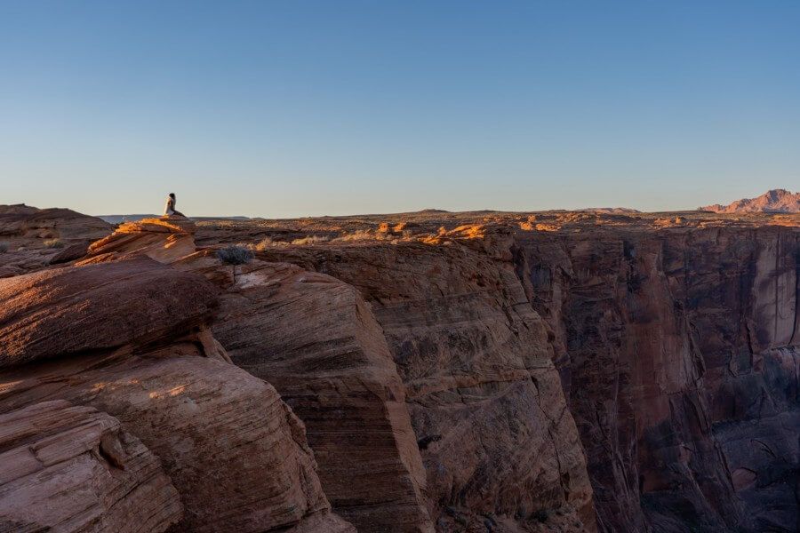 Lone hiker watching the sun come up in northern arizona sat on a cliff edge