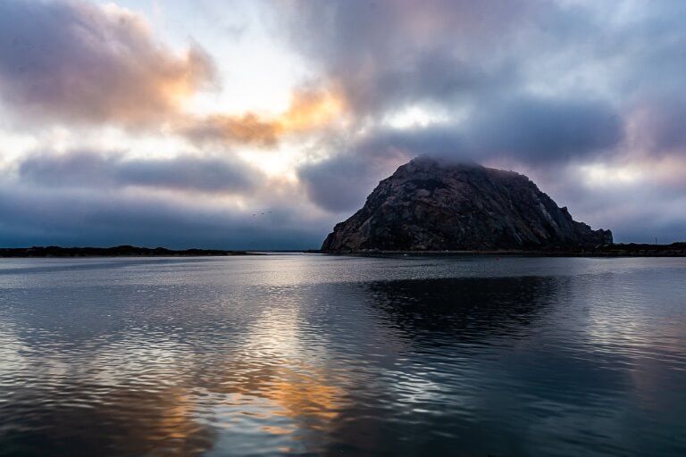 Morro Bay is an intriguing town between San Francisco and Los Angeles huge random rock at sea with colors in sky