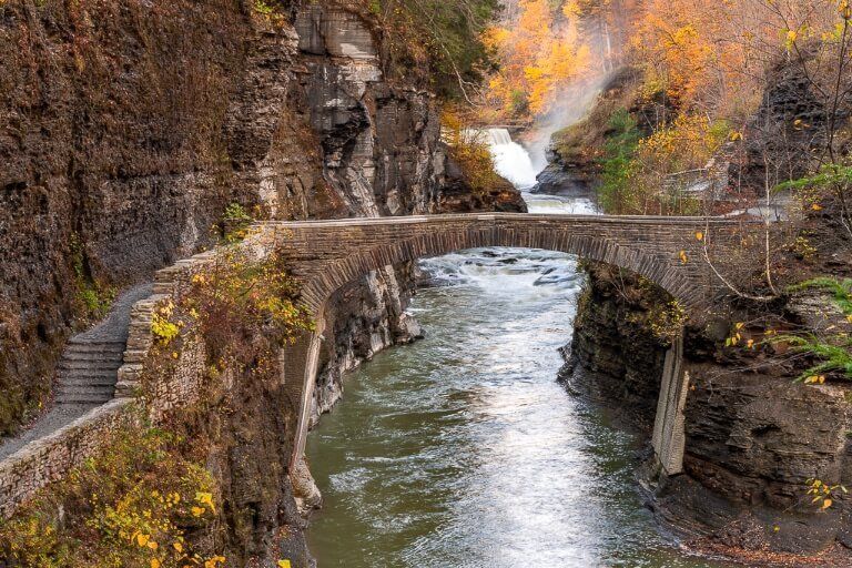 Letchworth State Park NY stone bridge crossing the Genesee River and Lower Falls waterfall in the background fall foliage colors photography