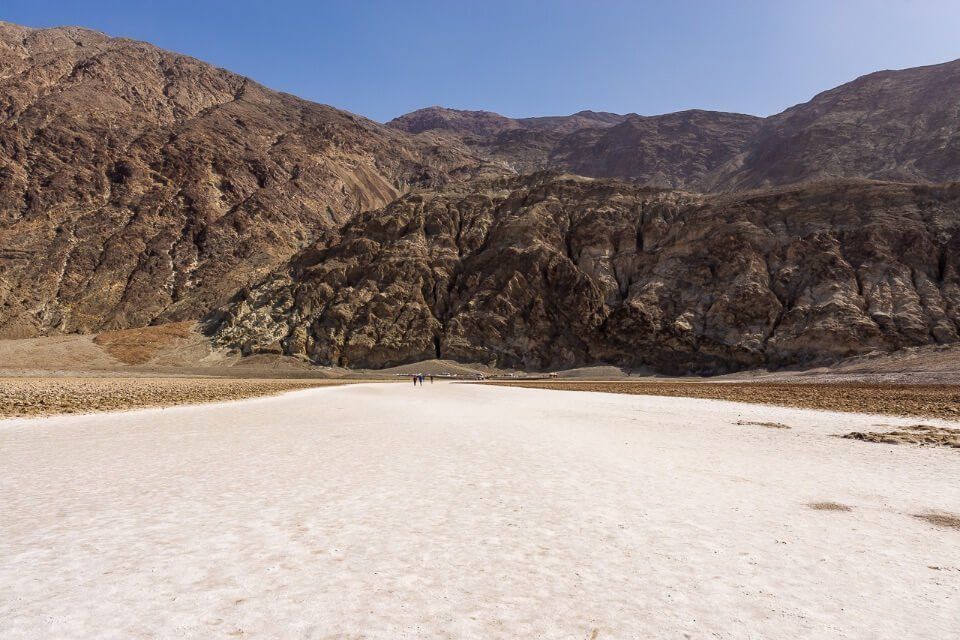 Badwater Basin is the most famous place to visit in death valley national park california white salt flat ground below sea level and huge rocks behind