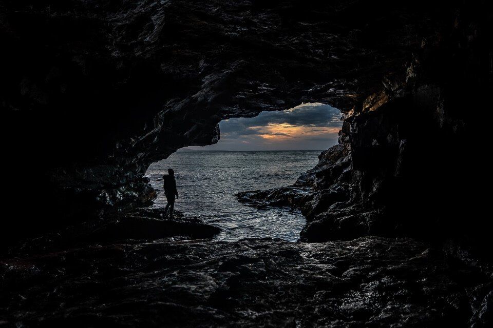 Kristen inside a cave silhouetted against the sunrise outside the cave at acadia national park maine usa