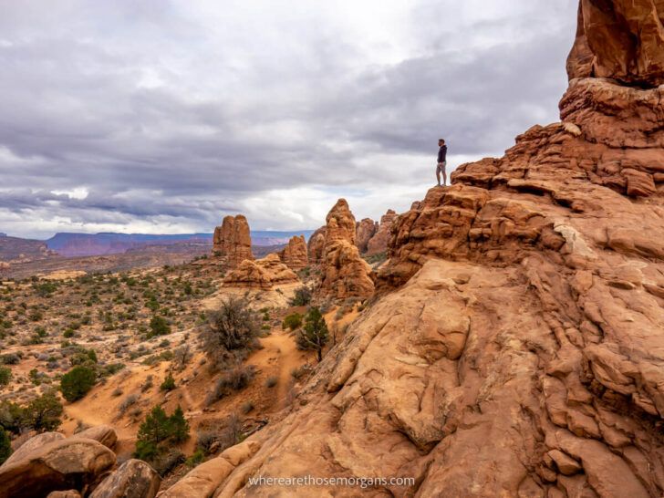 Hiker in distance on sandstone rock formations looking at a rocky landscape from one of the best hikes in Arches National Park in Utah
