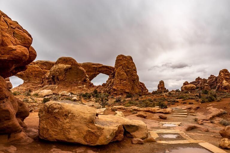 North and South Windows one of the most popular hikes in arches national park with a grey sky and orange rocks in utah
