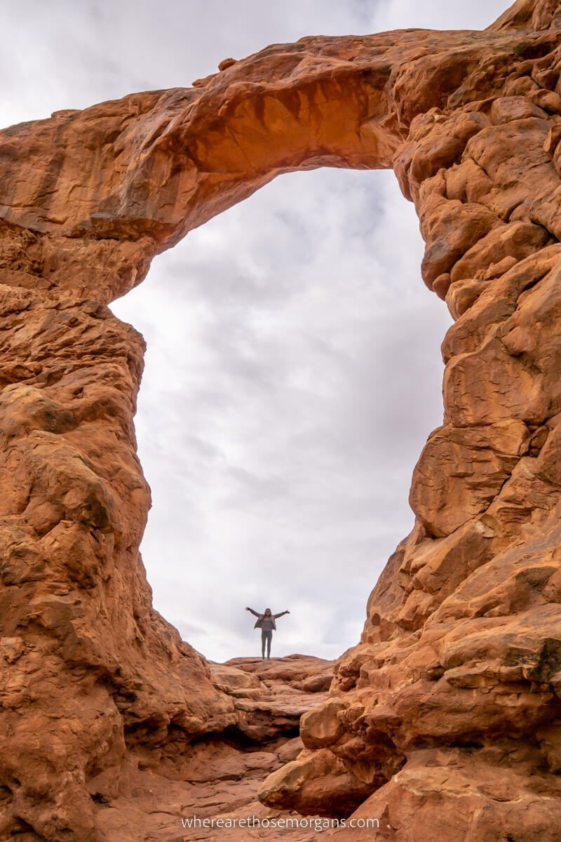 Woman stood underneath Turret Arch in Arches national park with arms raised