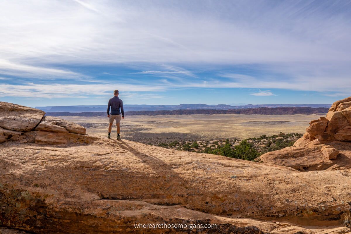Hiker looking out at a distant flat land from orange sandstone formations in Utah