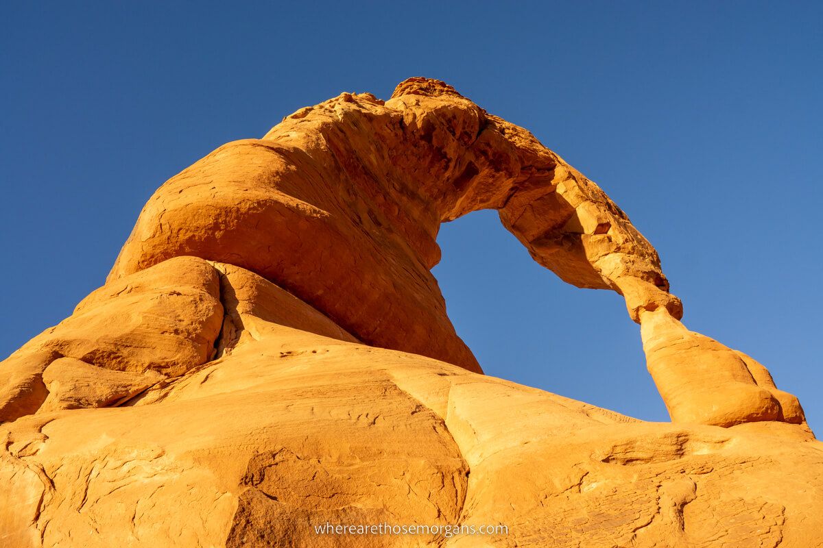 Photo looking up at a huge natural sandstone arch with a deep blue sky background in Arches National Park