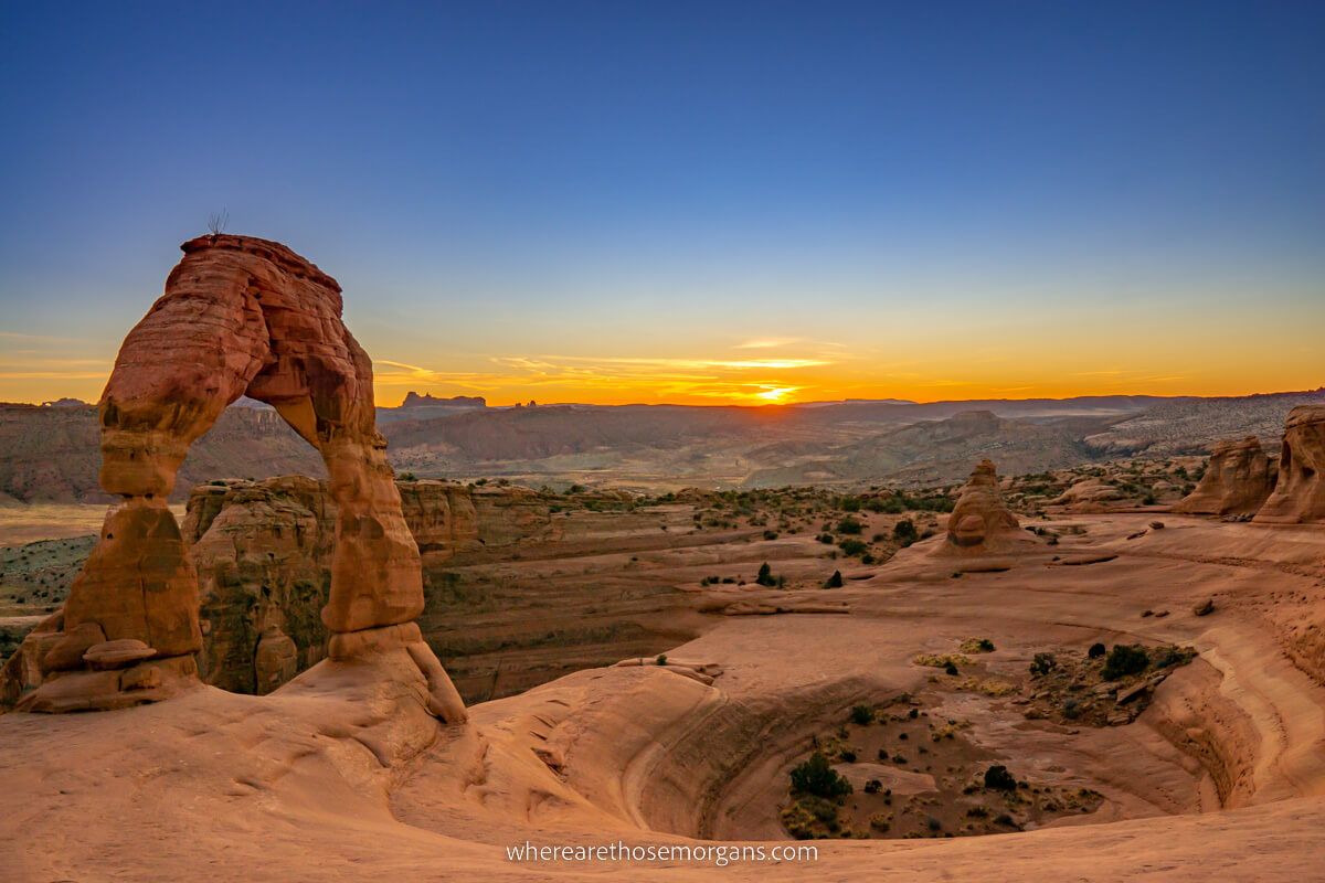 Stunning sunset at Delicate Arch in Arches National Park with a deep blue sky contrasting against oranges and yellows on the horizon