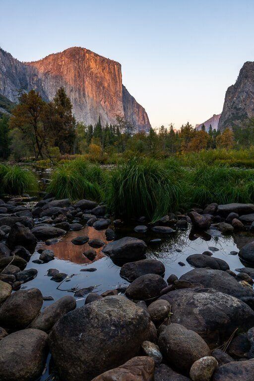 Serene sunrise at valley view in yosemite valley el capitan glowing red and reflecting in merced river with rocks