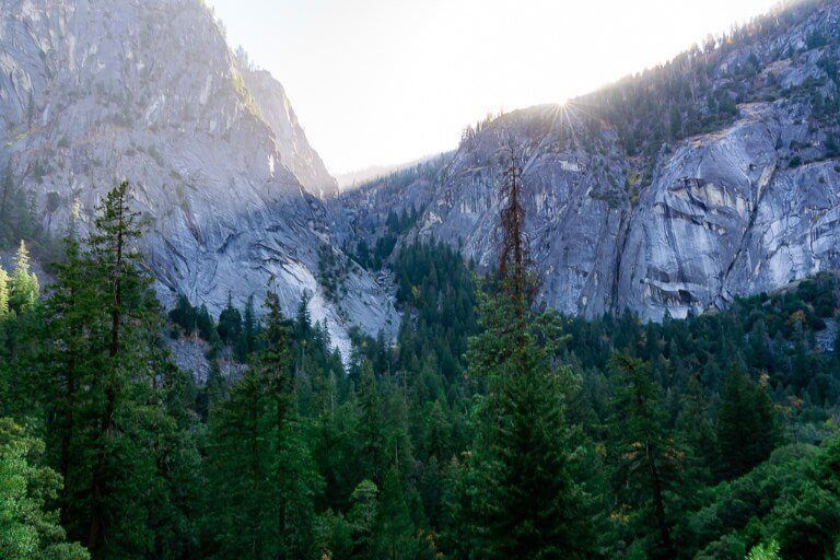 Starburst with the sun appearing over a granite wall with dense green trees in a valley and hazy sky Mist trail photography in yosemite national park california